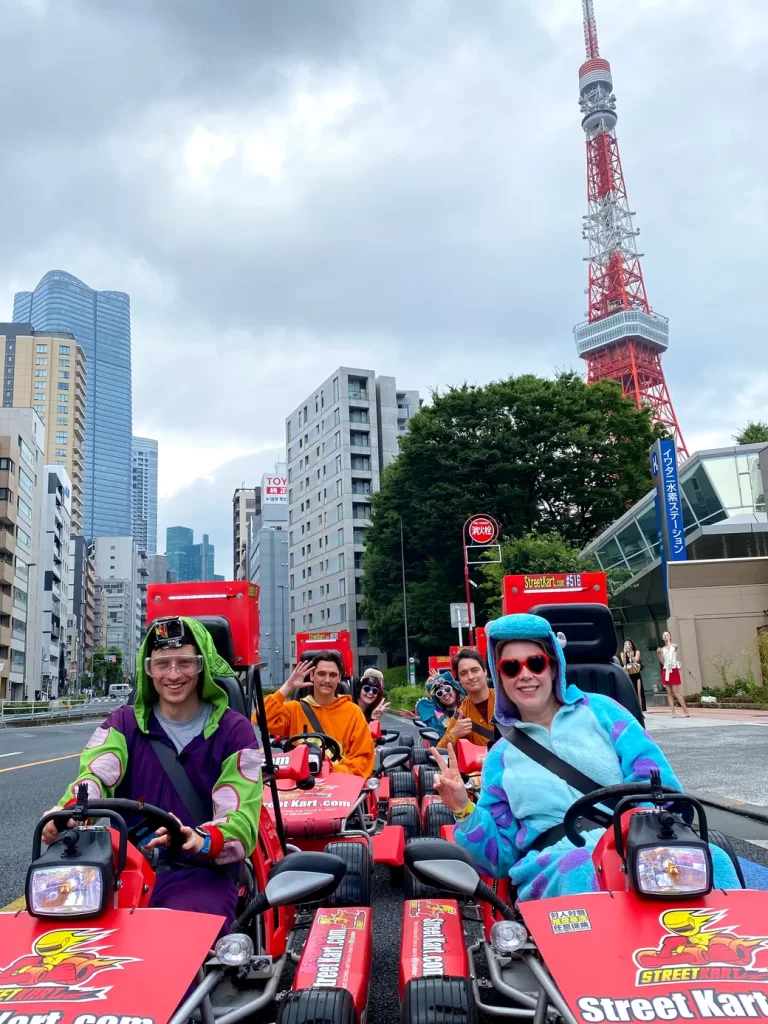 Group of friends in red go-karts riding down a city street with Tokyo Tower in the background.